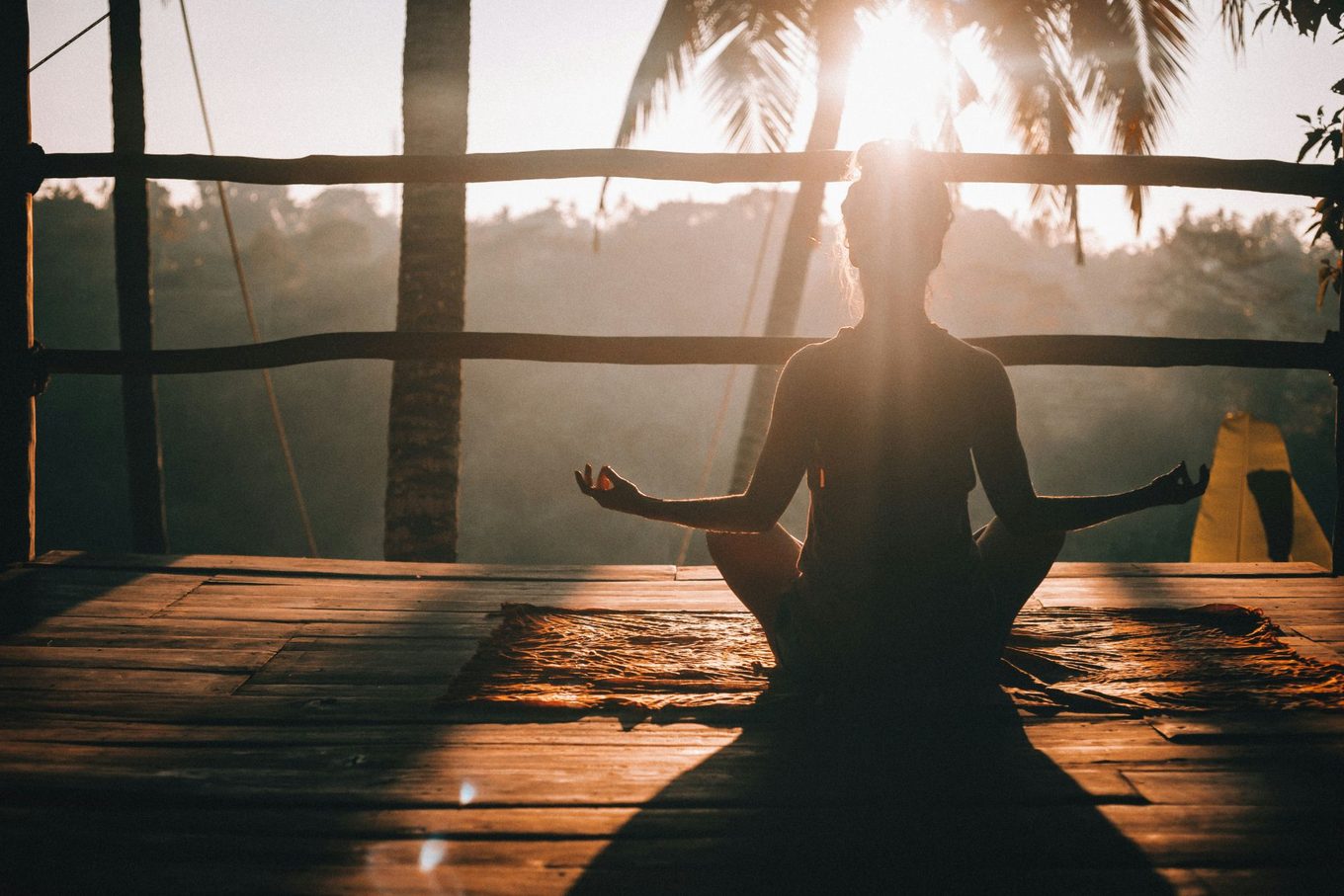 A person meditating on a wooden deck at sunrise