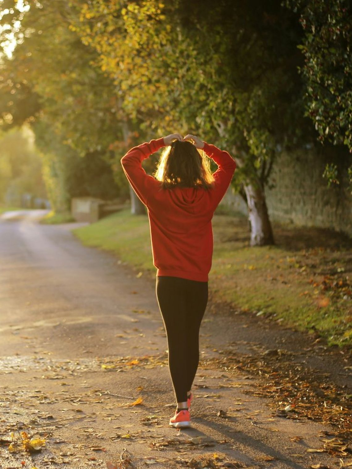 A woman walking on a tree-lined road at sunrise